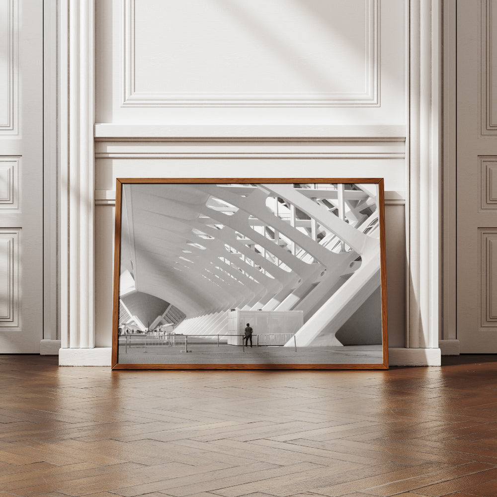Struttura architettonica moderna con grandi arcate bianche e design geometrico, illuminata dalla luce del giorno. Una persona in piedi vicino a una recinzione guarda l'edificio, con piccoli gruppi di persone visibili in lontananza.